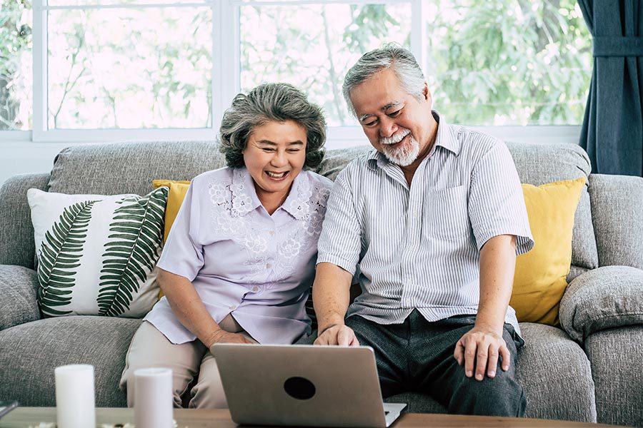 Blog - Senior Couple Smile and Use a Computer at Their Coffee Table While Sitting on a Couch in Their Sunny Living Room