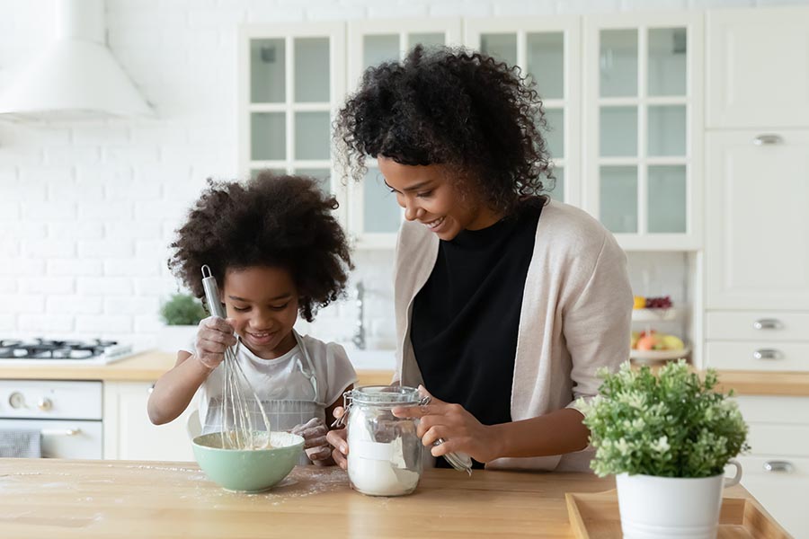 Personal Insurance - Mother and Young Daughter Bake Together in Their Bright White Kitchen